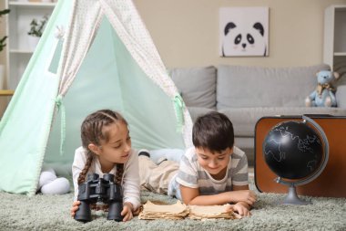 Evde dürbünlü şirin çocuklar halıda macera kitapları okuyorlar.