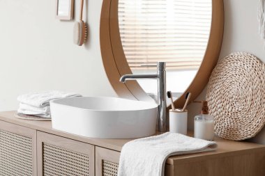 Banyodaki bej duvarın yanında lavabo, havlu ve banyo malzemeleri olan çekmeceler.