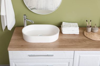 Küvet ve banyo aksesuarları olan çekmeceler şık bir banyoda yeşil duvarın yanında.