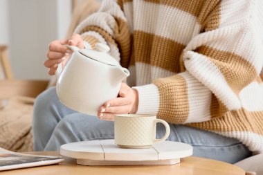 Evdeki masada fincana çay dolduran genç kadın, yakın plan.