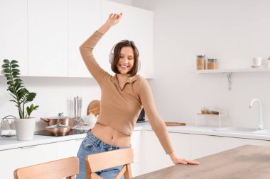 Kulaklıklı genç bir kadın mutfakta dans ediyor.