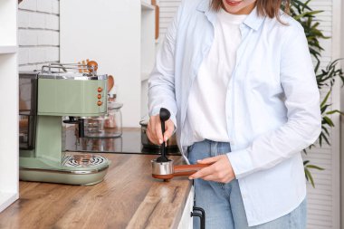 Genç bir kadın mutfakta kahve makinesiyle kahve yapıyor.