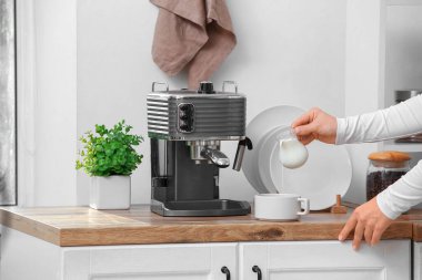 Genç bir kadın mutfaktaki sıcak kahveye taze süt döküyor.