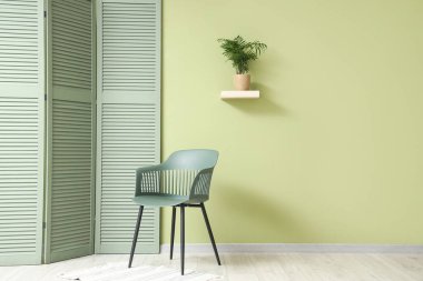 Sandalye, katlanan ekran ve odadaki yeşil duvarda rafta duran çiçek.