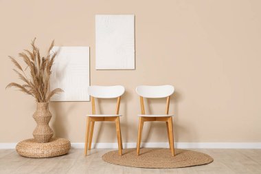 Sandalyeler, vazodaki otlar ve odadaki bej duvardaki resimler.