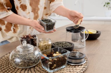 Mutfaktaki masada çay yapraklarını çaydanlığa koyan genç kadın, yakın plan.