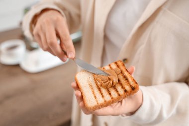 Genç bir kadın mutfakta bıçakla fıstık ezmesini tostun üstüne sürüyor.