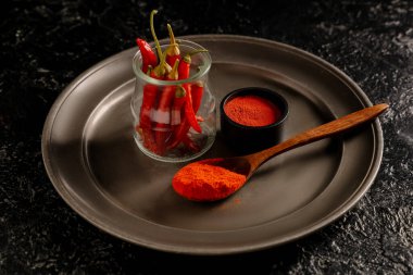 Ahşap kaşık kırmızı biber tozu ve siyah arka planda biberli kavanoz.