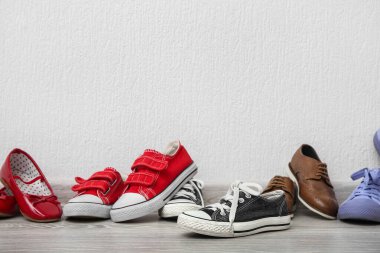 Beyaz duvarın yanında yerde farklı çocuk ayakkabıları var.