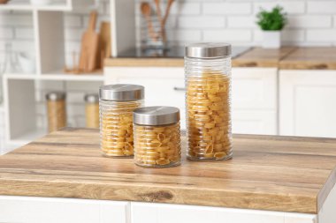 Mutfak masasında çiğ makarna kabukları olan farklı kavanozlar.