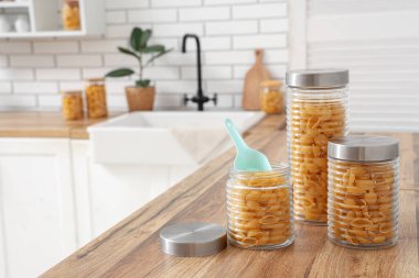 Mutfak masasında çiğ makarna kabukları olan farklı kavanozlar.