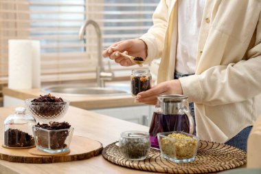 Mutfaktaki masada amberçiçeği çayı demleyen genç kadın, yakın plan.