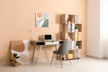 Bej duvarın yanında masa, sandalye ve raf ünitesi olan oda.