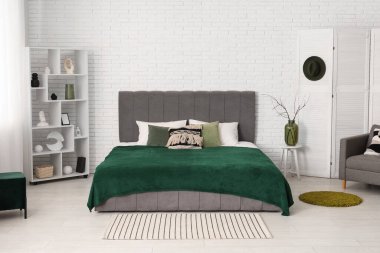 Yatak odasının içinde, beyaz tuğla duvarın yanında yatak, katlanan ekran ve raf ünitesi var.