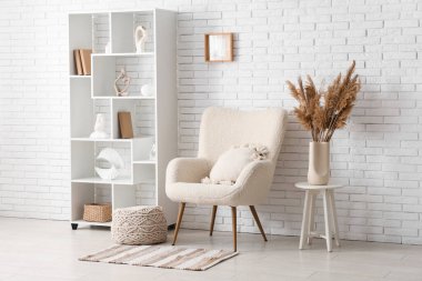 Beyaz tuğla duvarın yanında koltuk, puf ve raf ünitesi olan bir oda.