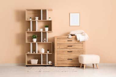 Bej duvarın yanında çekmeceler, puf ve raf üniteleri olan bir oda.