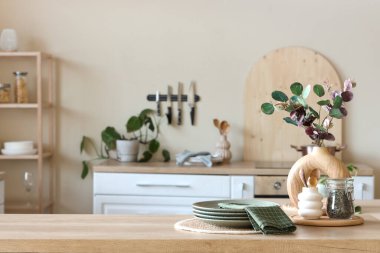 Mutfaktaki masada okaliptüs dalları, tabaklar ve peçeteli vazo.