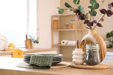 Mutfaktaki masada okaliptüs dalları, tabaklar ve peçeteli vazo.