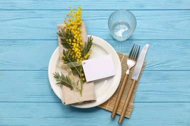 Boş bir kart ve mavi ahşap arka planda mimoza çiçekleri olan güzel bir masa.