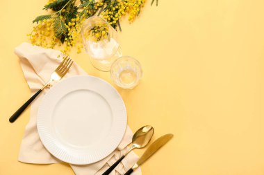 Altın çatal bıçak takımı ve sarı arka planda mimoza çiçekleri olan güzel bir masa.