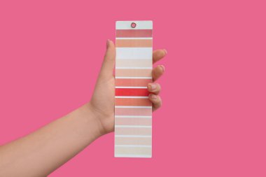 Pembe arka planda boya rengi paleti olan kadın el, yakın plan.