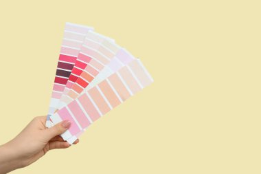 Sarı arka planda boya rengi paletleri olan kadın eli