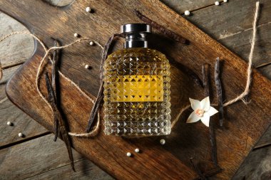 Parfüm şişesi, vanilya çubuğu ve tahta arka planda kesim tahtası olan kompozisyon