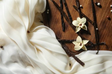 Tahta arka planda vanilya çubukları, çiçekler ve hafif kumaşla kompozisyon