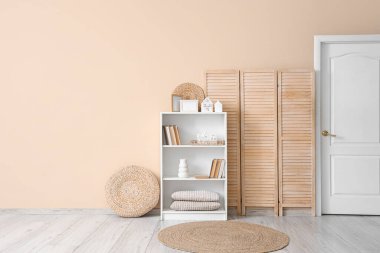 Resim çerçeveli raf ünitesi, kitaplar ve mum tutacakları bej duvarın yanındaki oda şeklinde.