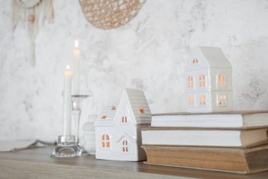 Ev şekilli mum tutucular ve kitaplar oturma odasındaki beyaz grunge duvarının yanında, yakın plan.