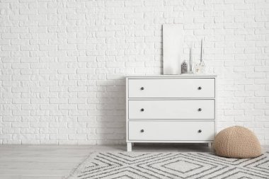 Beyaz tuğla duvarın yanındaki çekmecelerde ev şeklinde mum tutucuları olan odanın içi.