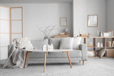 Masanın üzerinde ev şeklinde mum tutacakları olan aydınlık oturma odasının içinde.