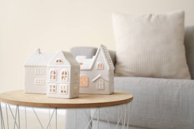 Bej duvarın yanındaki masada ev şeklinde mum tutucular var.