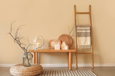 Ev şeklinde mum tutucular, fotoğraf çerçevesi ve hasır halı oturma odasındaki bej duvarın yanında.