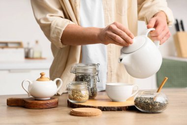 Genç adam mutfaktaki masaya çay koyuyor, yakın plan.