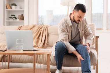 Evdeki kanepede diz ağrısı çeken genç bir adam.