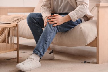 Evdeki kanepede diz ağrısı çeken genç bir adam.