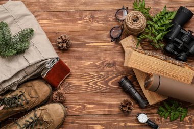 Ahşap arka planda farklı seyahat öğeleri, ayakkabılar, giysiler ve çam kozalakları ile kompozisyon