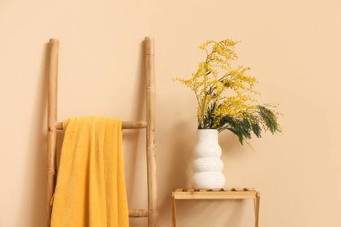 Rafta mimoza çiçekli vazo ve bej duvarın yanında merdiven.