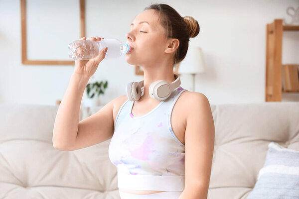 Sporty young woman drinking water  at home