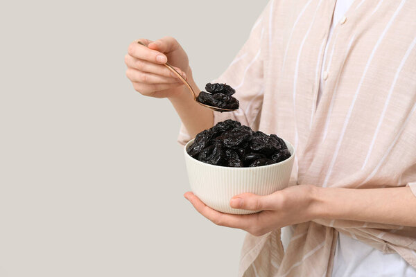 Woman holding bowl and spoon with dried prunes on grey background, closeup