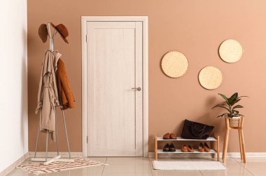 Elbise askısı ve modern koridorun içindeki kahverengi duvarın yanında duran ayakkabılar.