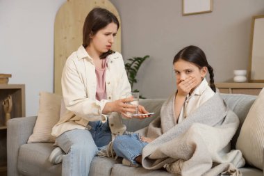 Evdeki kanepede annesinden ilaç alan hasta bir kız.