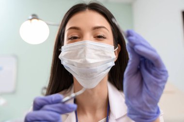 Klinikte tıbbi maskesi ve aletleri olan genç bayan dişçi, yakın plan.
