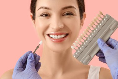 Gülümseyen genç kadın ve dişçi pembe arka planda diş rengi örnekleri, yakın plan