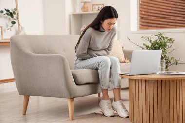 Evdeki kanepede karın ağrısı çeken genç bir kadın.