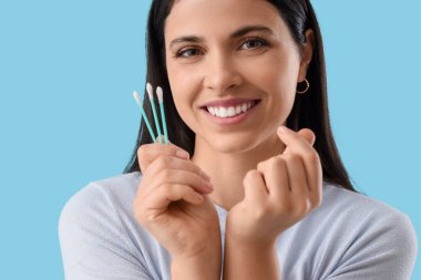 Pamuk tomurcuklu güzel bir kadın mavi arka planda kalp hareketi yapıyor, yakın plan.