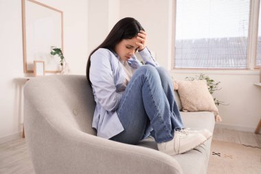 Evdeki kanepede kendini kötü hisseden genç bir kadın.