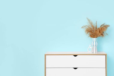 Mavi duvarın yanındaki klozette otlu vazo ve heykel var.