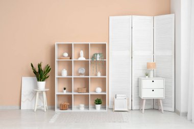 Oturma odasının içinde beyaz raf ünitesi, katlanır ekran ve masa